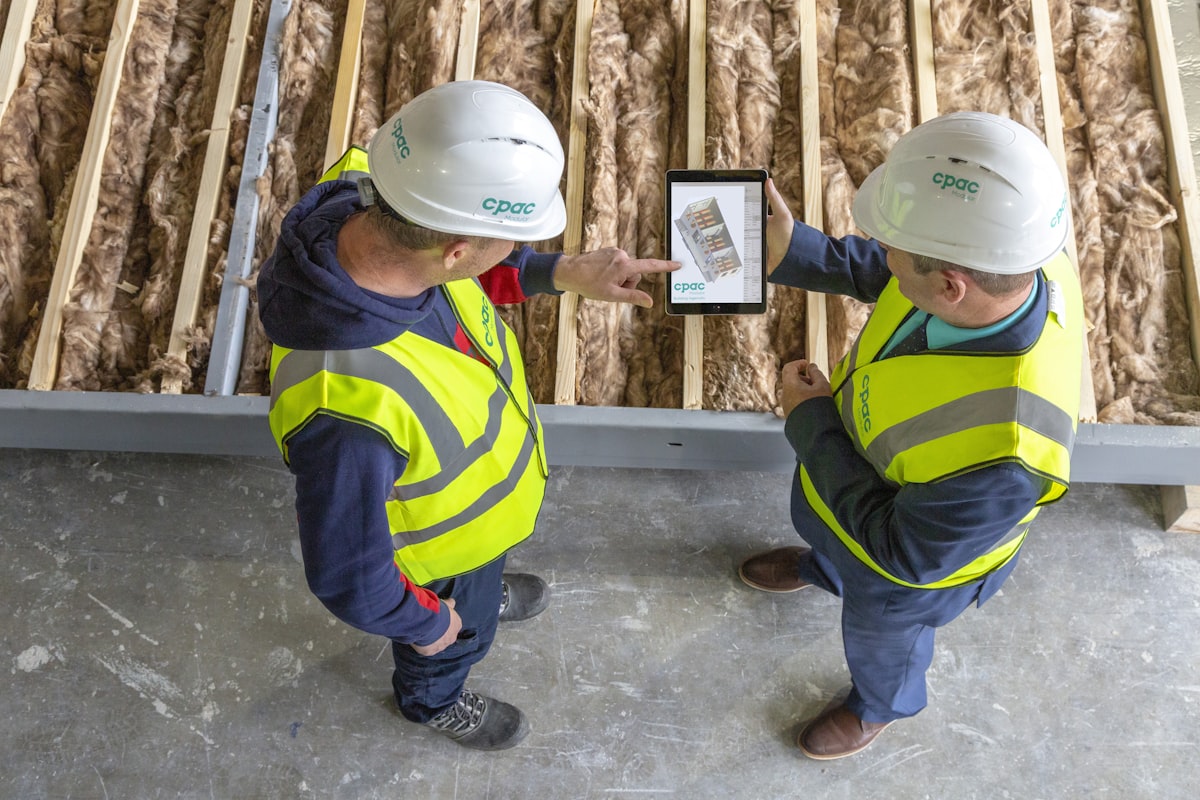 Two inspectors reviewing jobsite compliance data on a tablet against an insulated wall assembly.