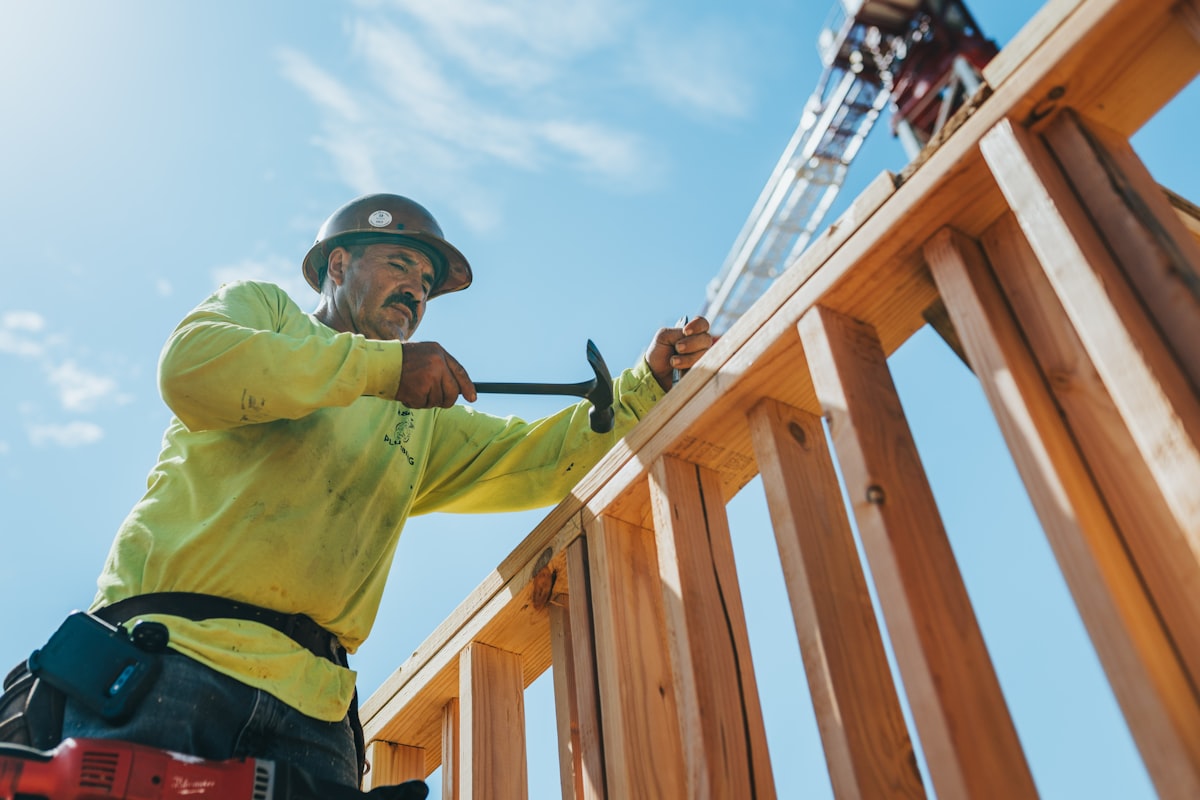 A framing carpenter in hi-vis working steel and timber on an active site, a tower crane behind.